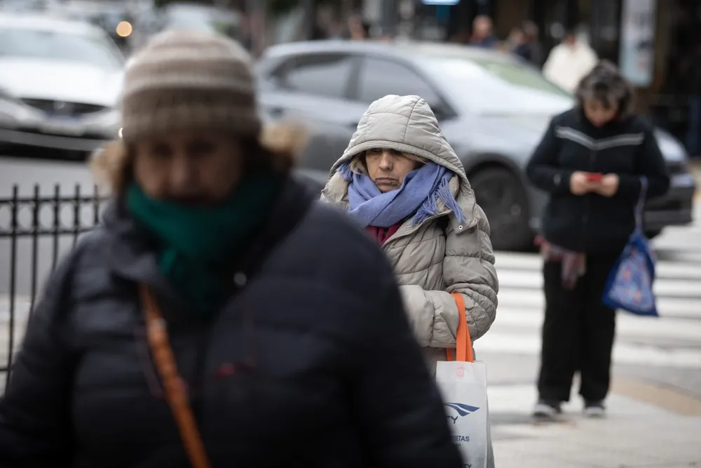 Personas portan ropa abrigadora mientras caminan por una calle durante una ola de frío, en la ciudad de Buenos Aires
